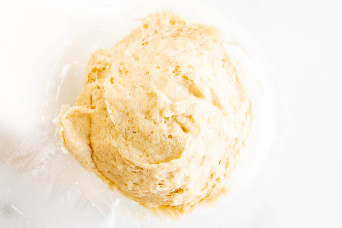 A bowl of dough for baking homemade Cookie Butter Cinnamon Rolls in a white bowl.