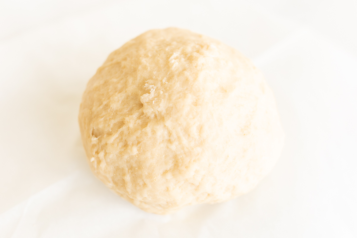 A ball of dough, infused with the flavors of cookie butter and cinnamon, sitting on a white surface.