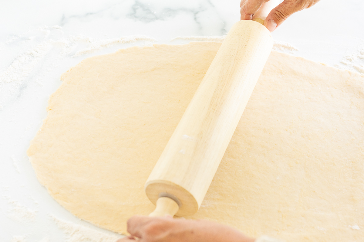A person rolling out dough with a rolling pin to make Cookie Butter Cinnamon Rolls.