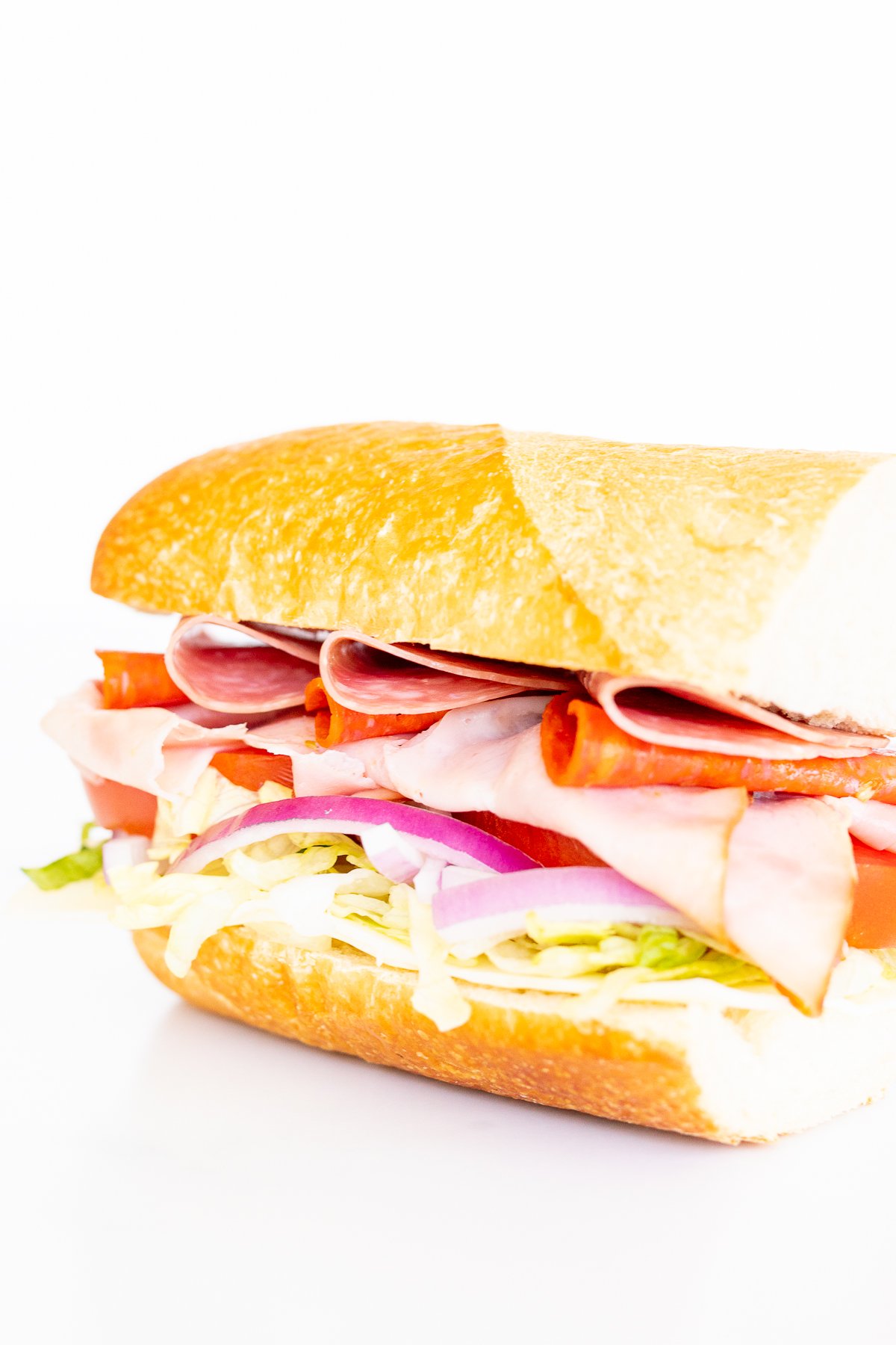 A sandwich with ham, lettuce, tomatoes, and onions.
