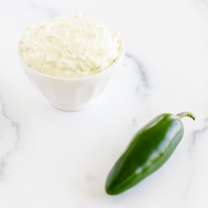 A white bowl with whipped cream and a jalapeno pepper topped with jalapeño cream cheese.