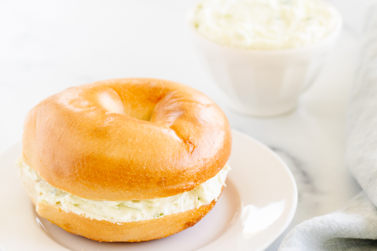 A bagel on a plate with a cup of Jalapeño Cream Cheese.