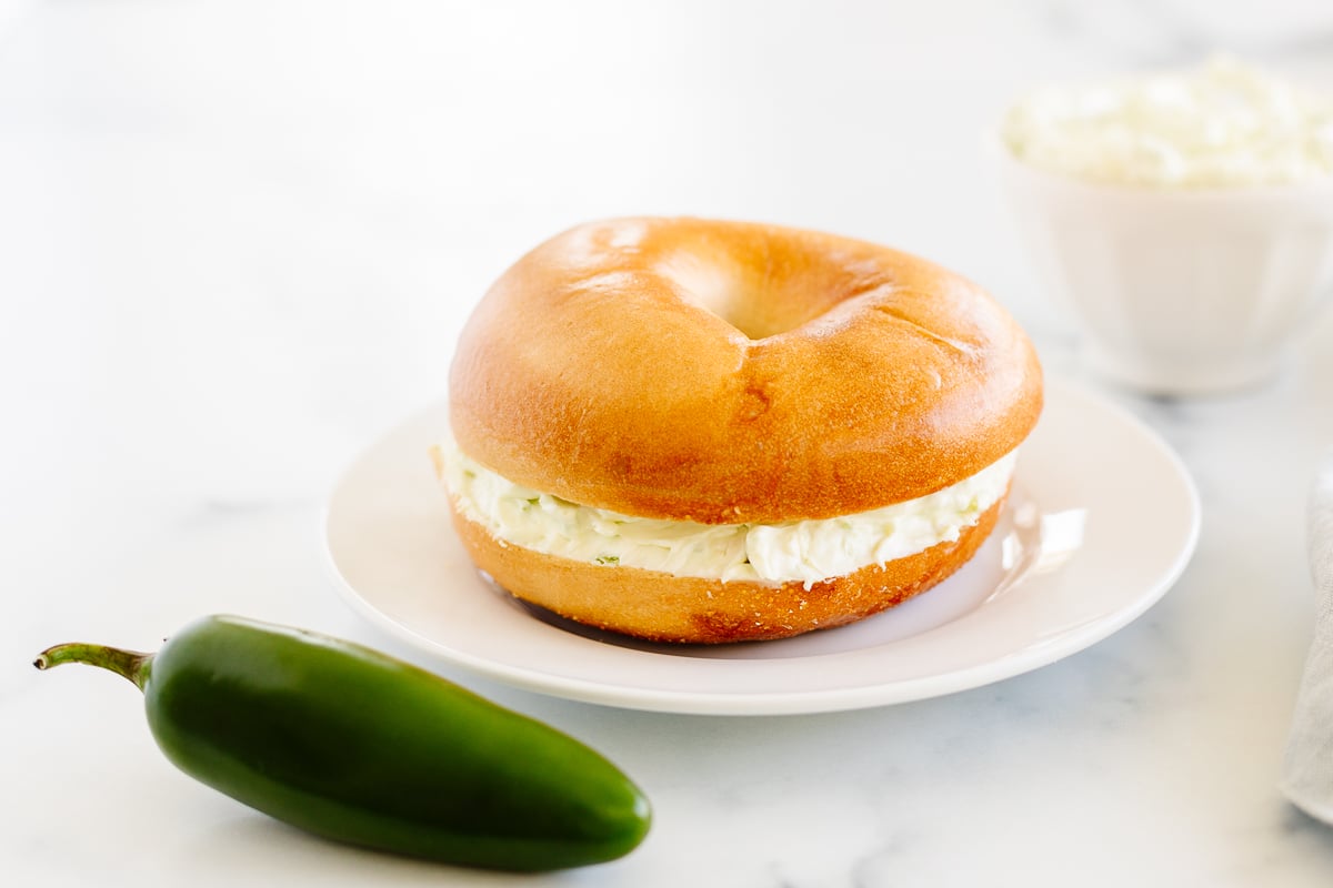 A white plate holds a delicious bagel topped with jalapeno cream cheese.