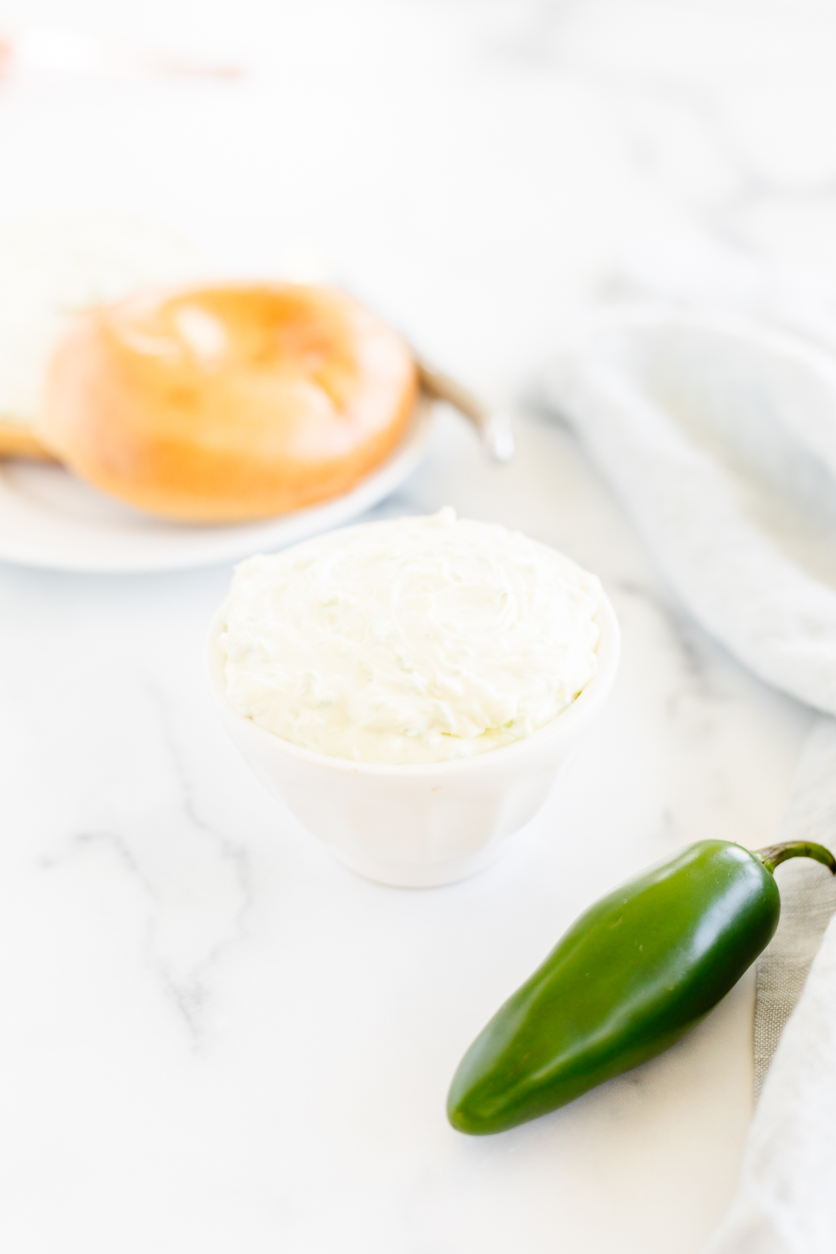 A bowl of sour cream with a jalapeno on a marble table.