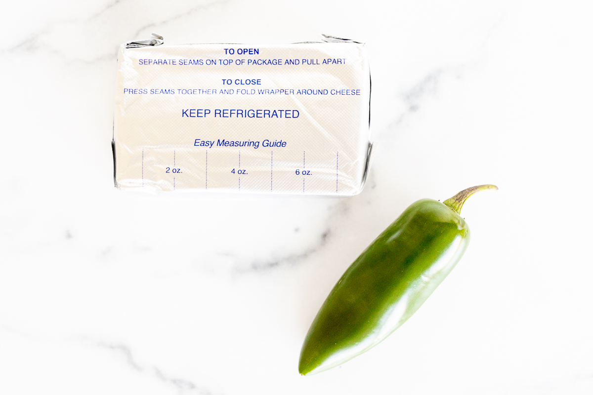 A green pepper next to a package of jalapenos filled with Jalapeno Cream Cheese.