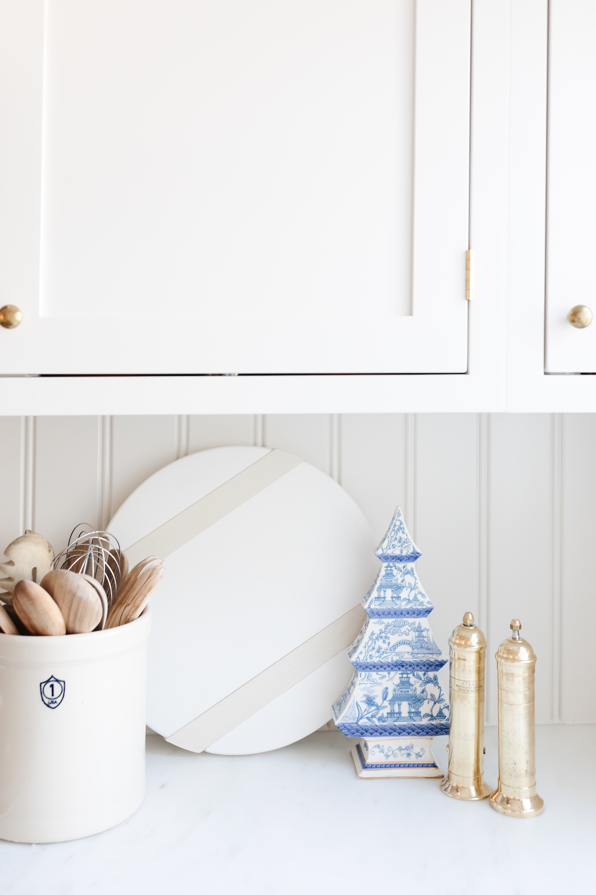A white kitchen counter with white cabinets and white objects filled with kitchen gifts.