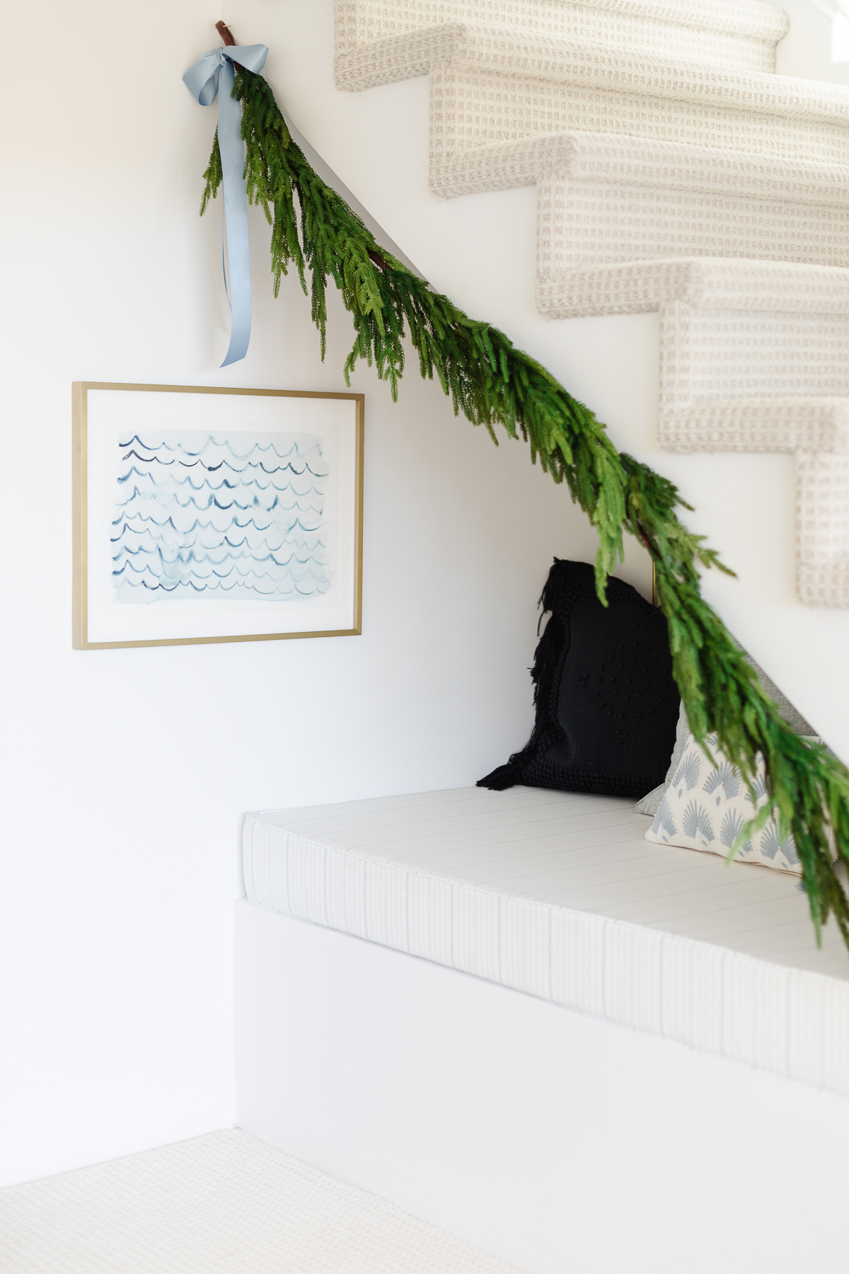 A christmas garland hangs under the stairs in a white home.