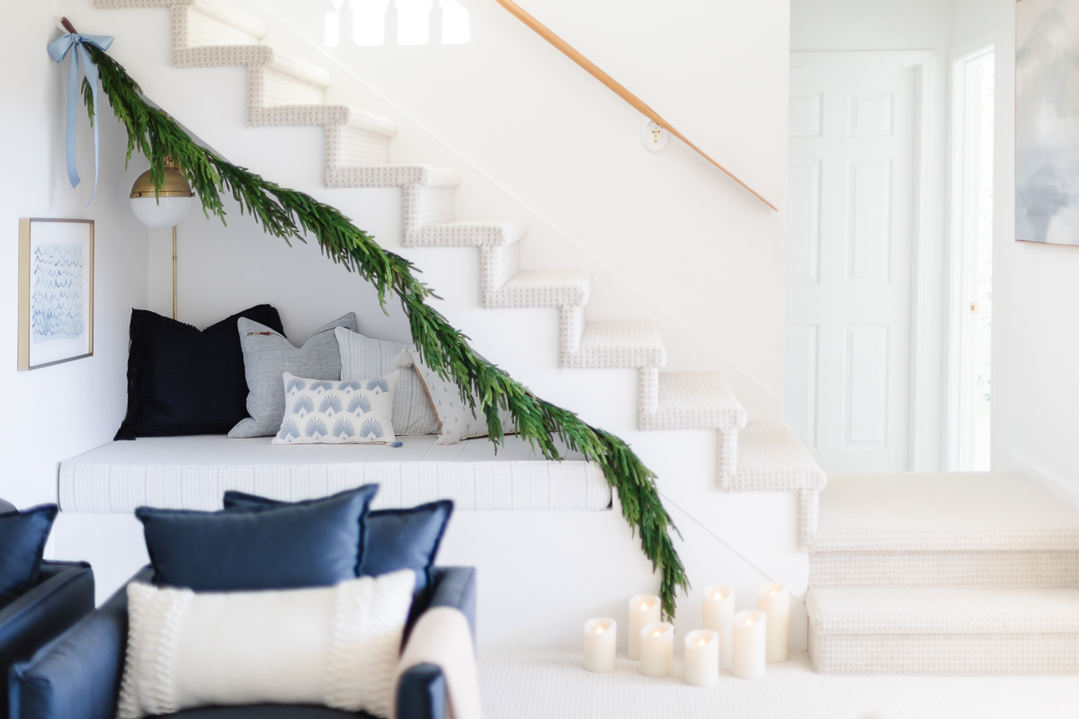 A white and blue living room with a christmas garland on the stairs.