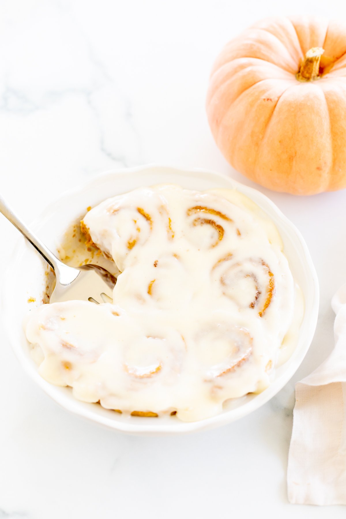 A plate of Pumpkin Cinnamon Rolls with cream cheese frosting.