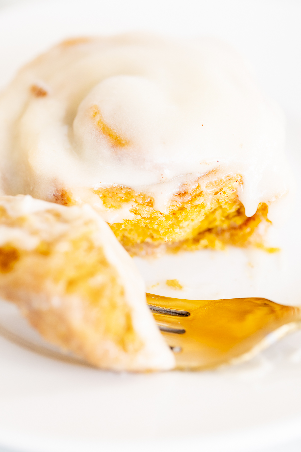 A pumpkin cinnamon roll on a plate with a fork.