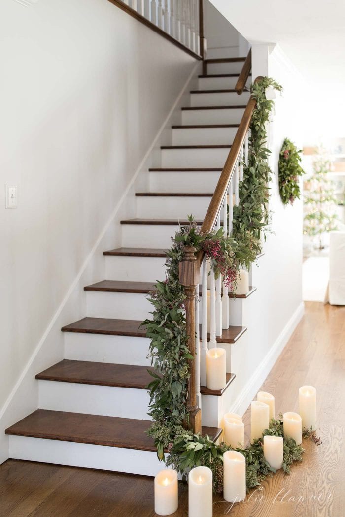 A cedar garland-adorned staircase illuminated by candles.