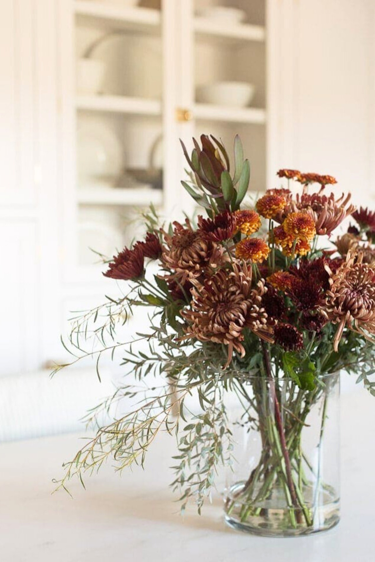 A Thanksgiving centerpiece of flowers on a table in a kitchen.