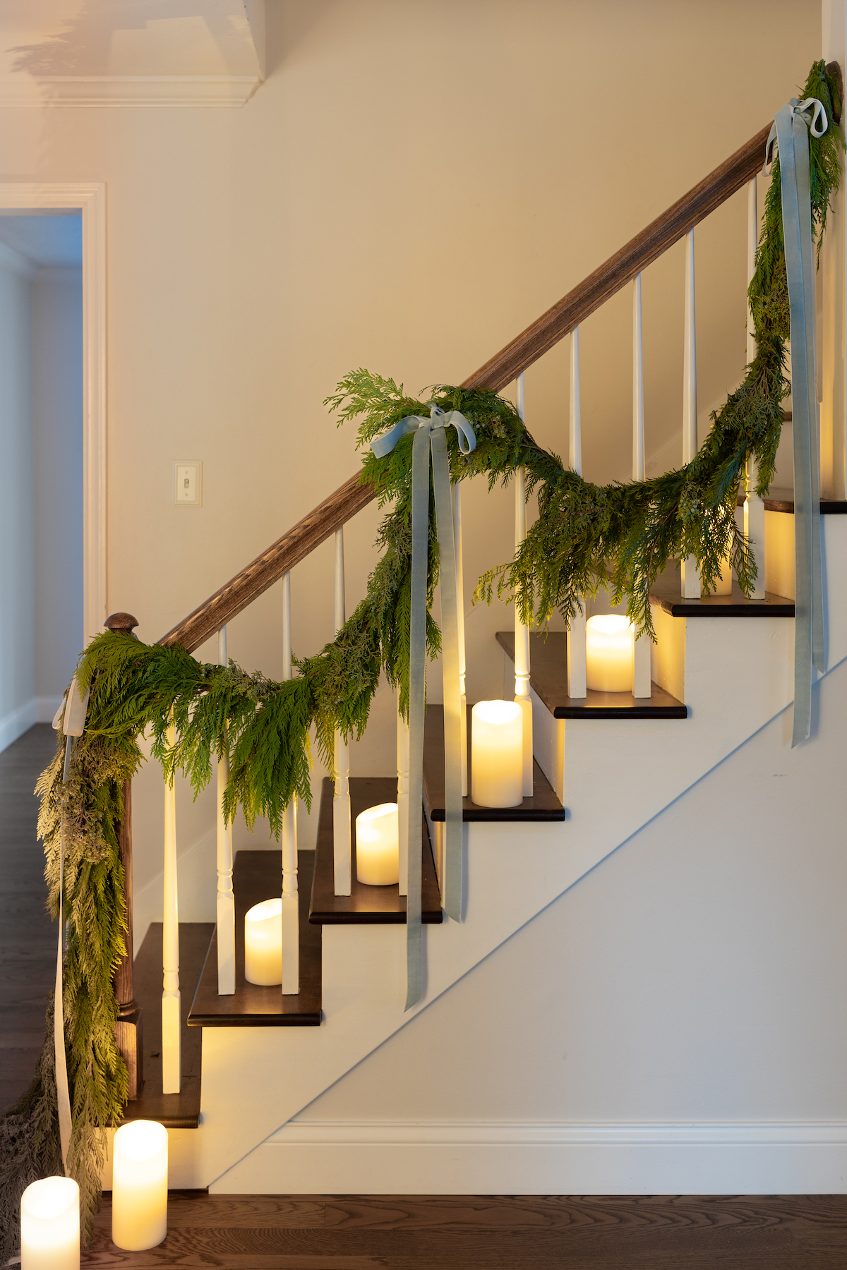A staircase decorated with greenery and battery operated candles.