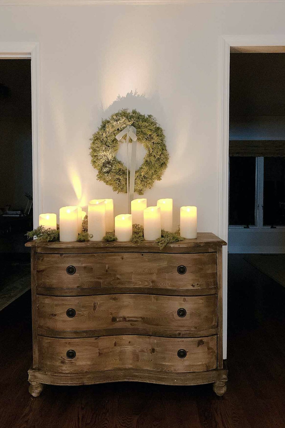 A dresser with LED candles and a wreath on it.