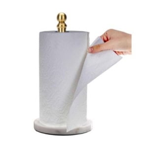 A hand elegantly pulls a sheet from a white paper towel roll on a marble base with a gold holder, enhancing kitchen counter organization.