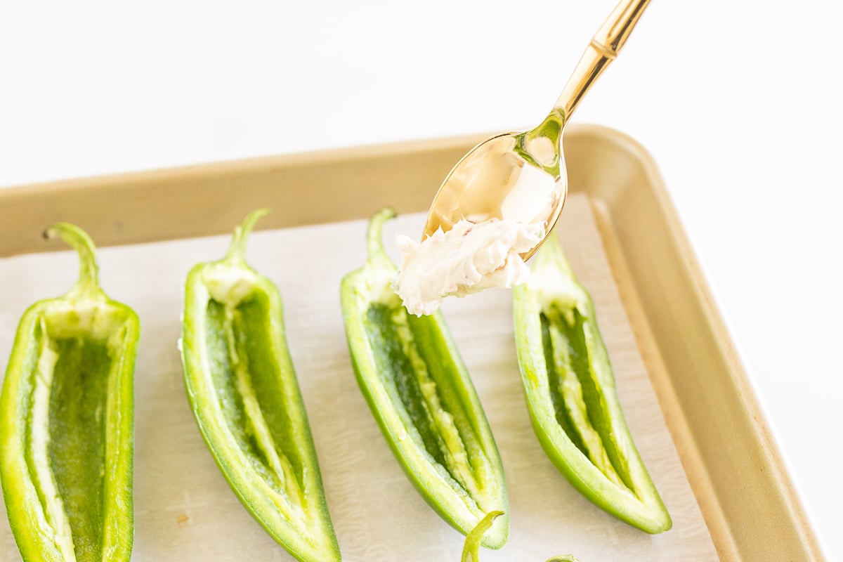 Green peppers on a baking sheet with a spoon.