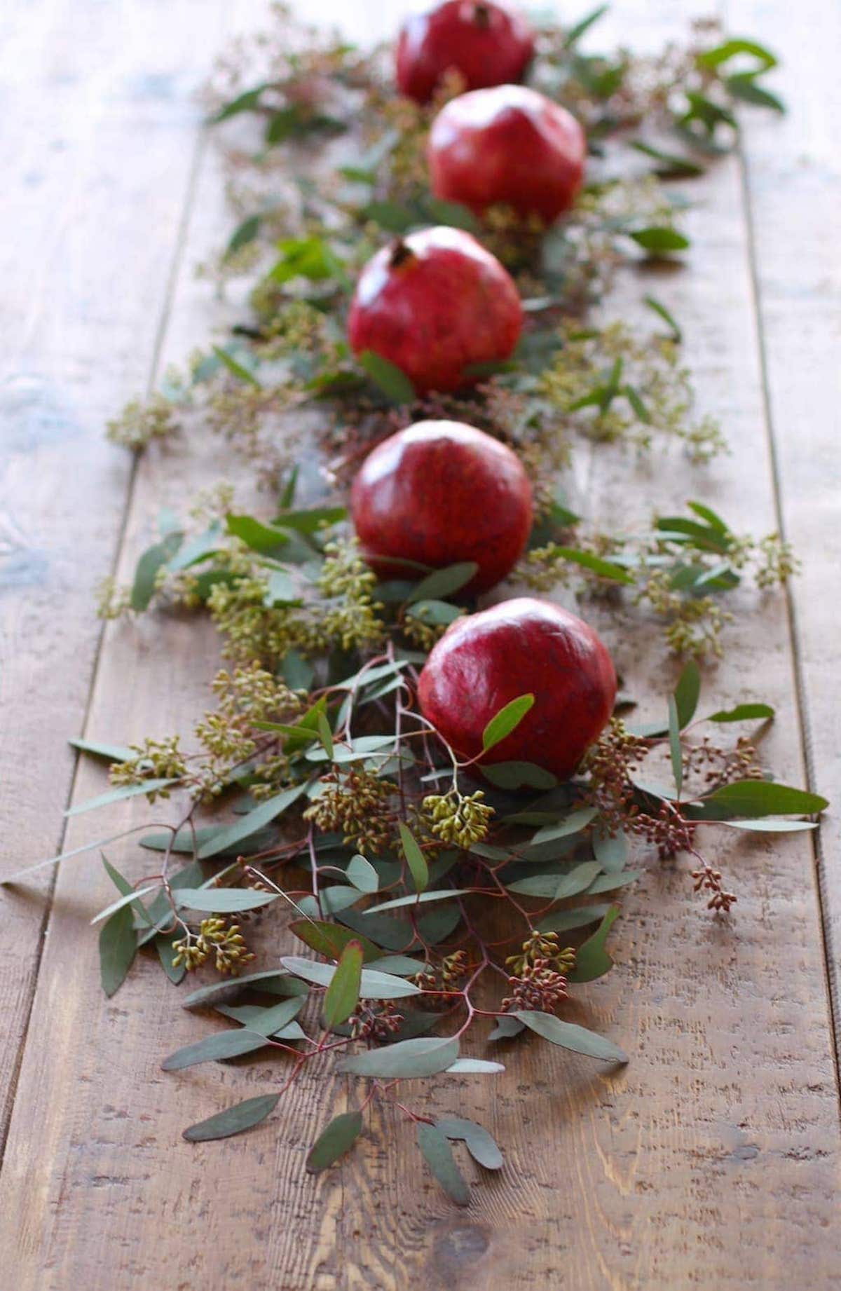Pomegranate and eucalyptus leaves create a stunning Christmas candle centerpiece on a wooden table.