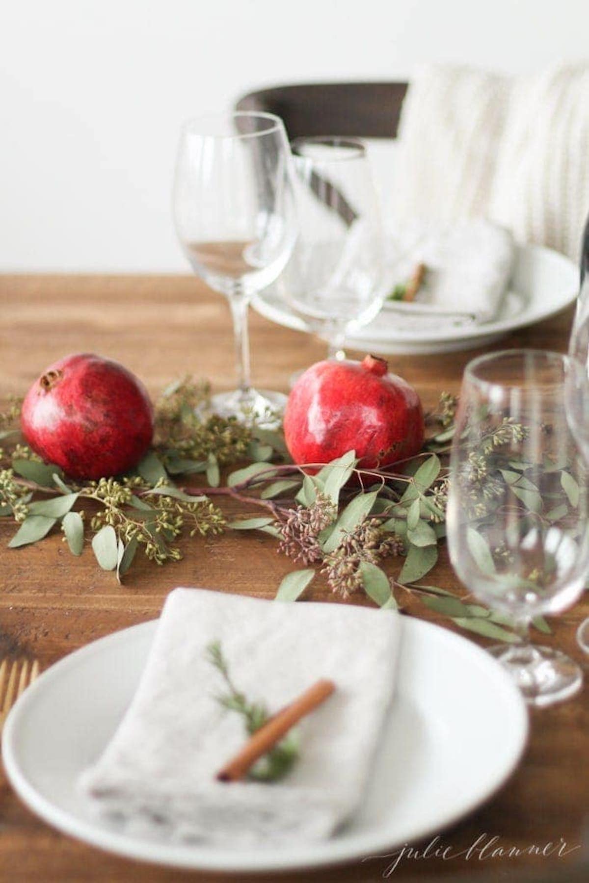 A table setting with a Christmas candle centerpiece, adorned with pomegranates and eucalyptus leaves.