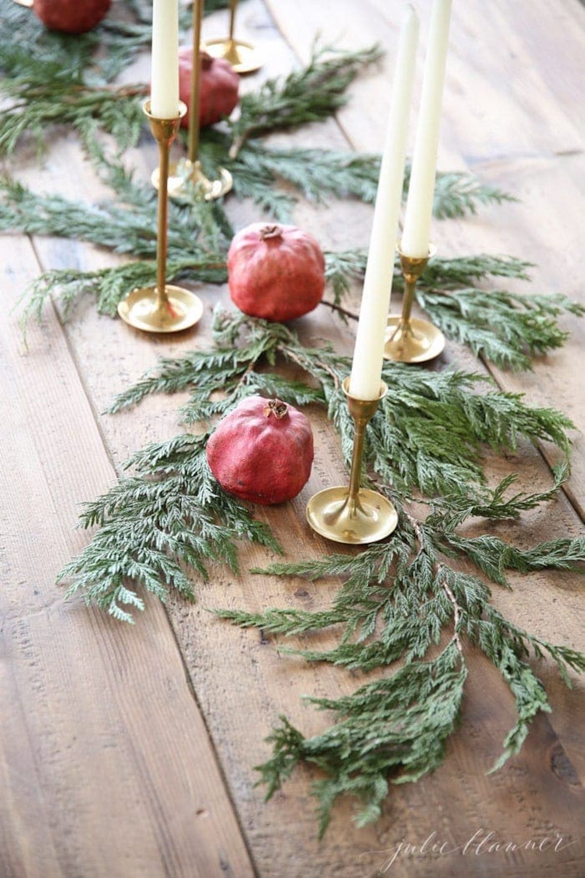 A festive Christmas centerpiece adorned with candles and pomegranates beautifully displayed on a rustic wooden table.