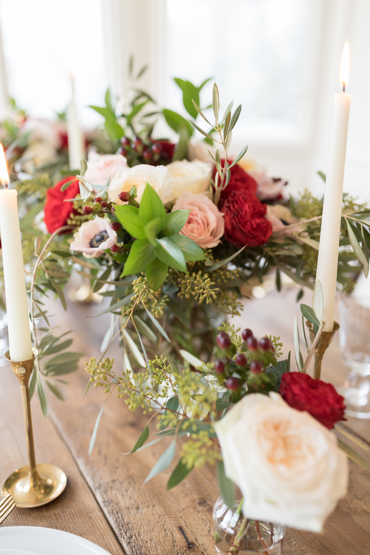 A Christmas centerpiece with flowers and candles on a wooden table.