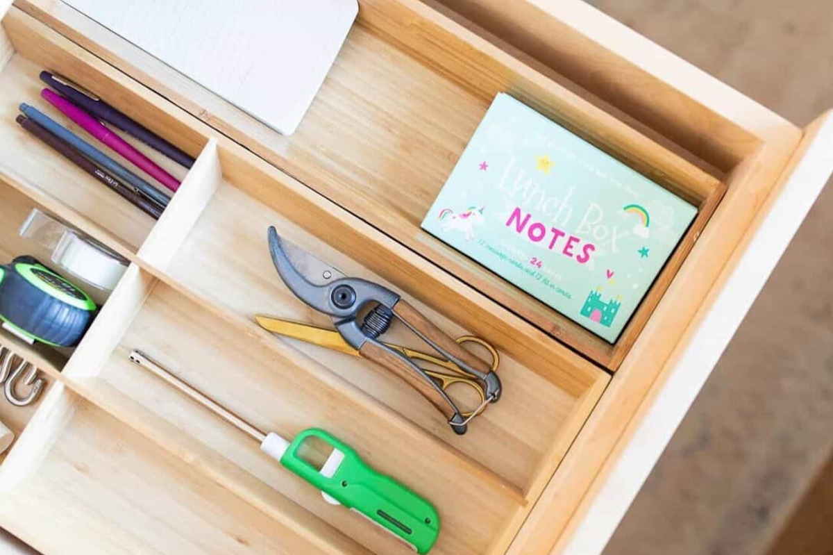 A wooden drawer with pens, pencils, and a notepad neatly organized in a drawer organizer.