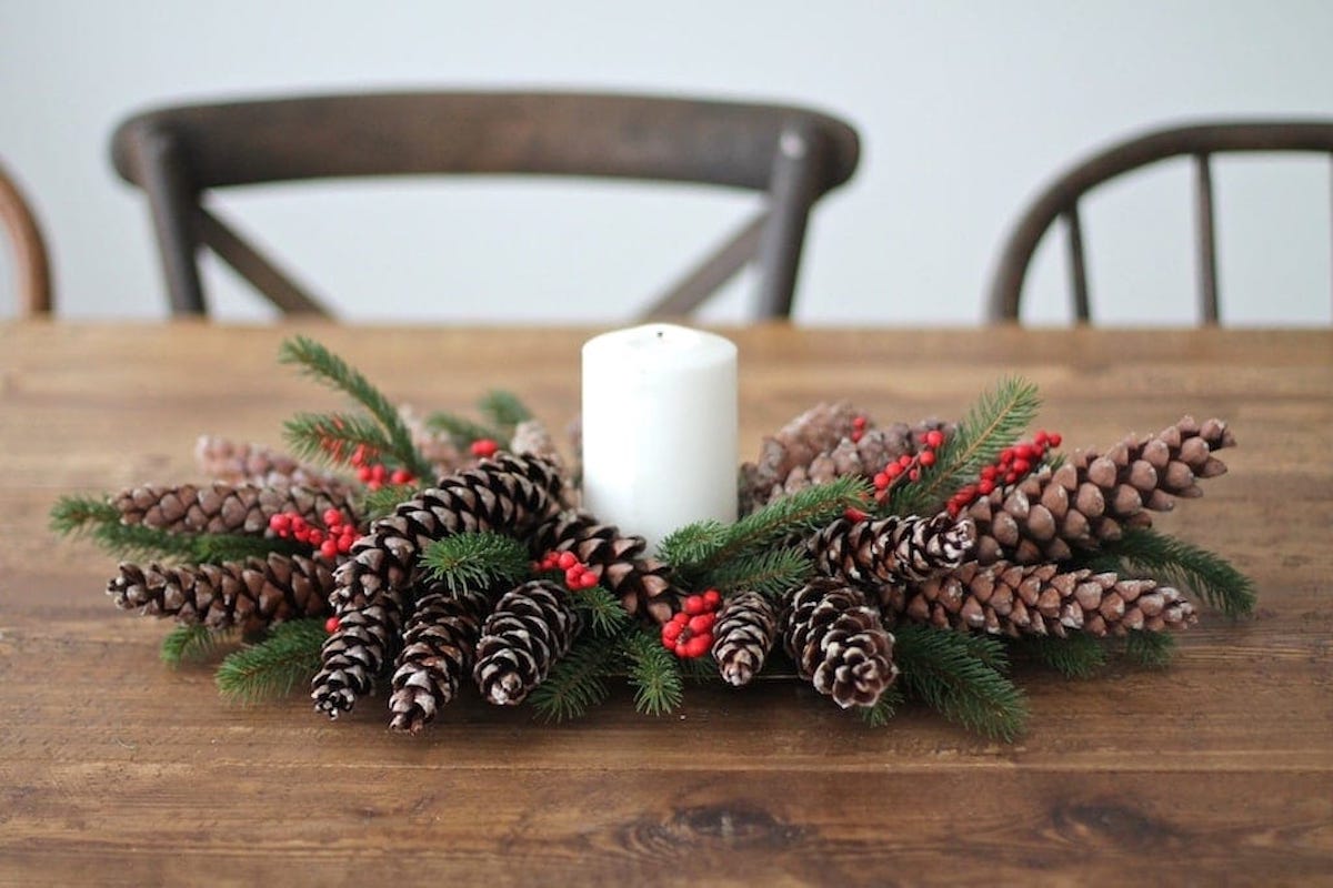 Christmas Centerpiece with Pine cones and berries, accompanied by a candle, creates a festive ambiance on a table.