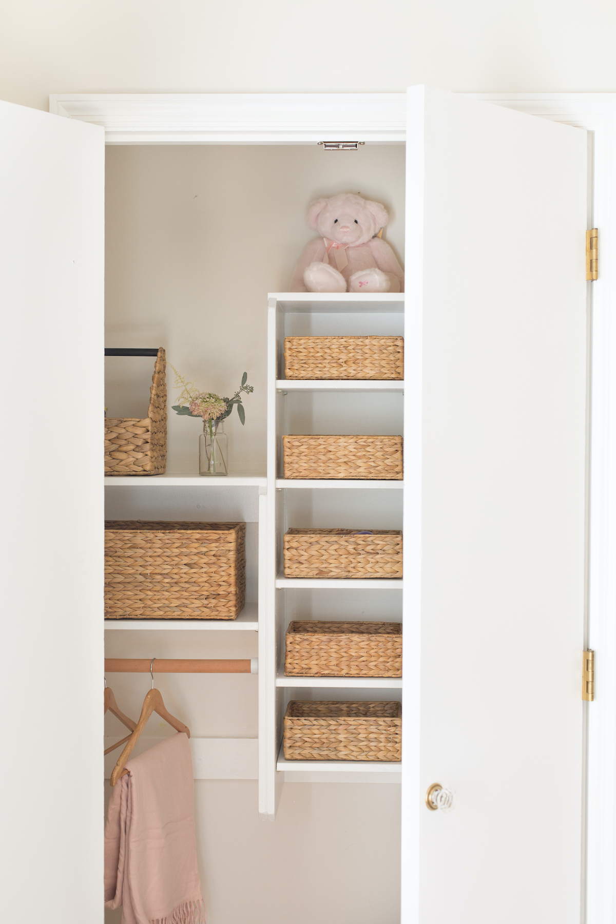 A white closet with wicker baskets for home organization and a teddy bear.