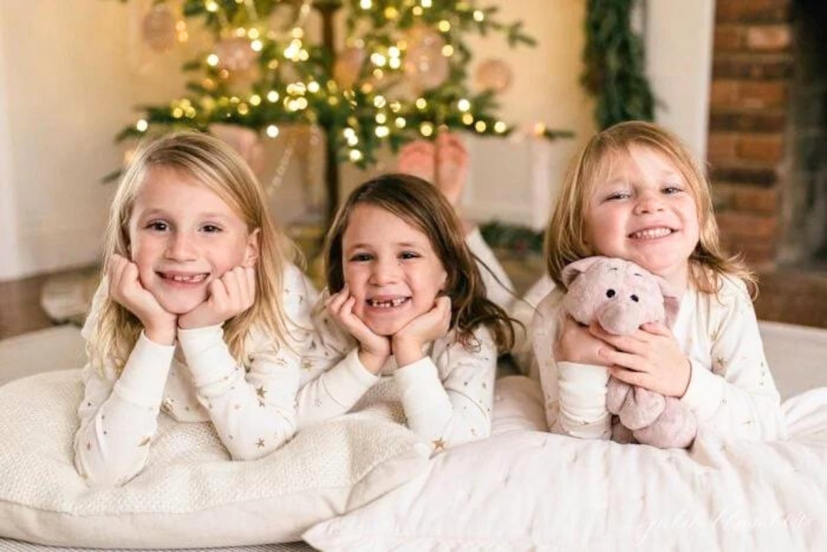 Three girls in pajamas laying on the floor in front of a Christmas tree in their house.