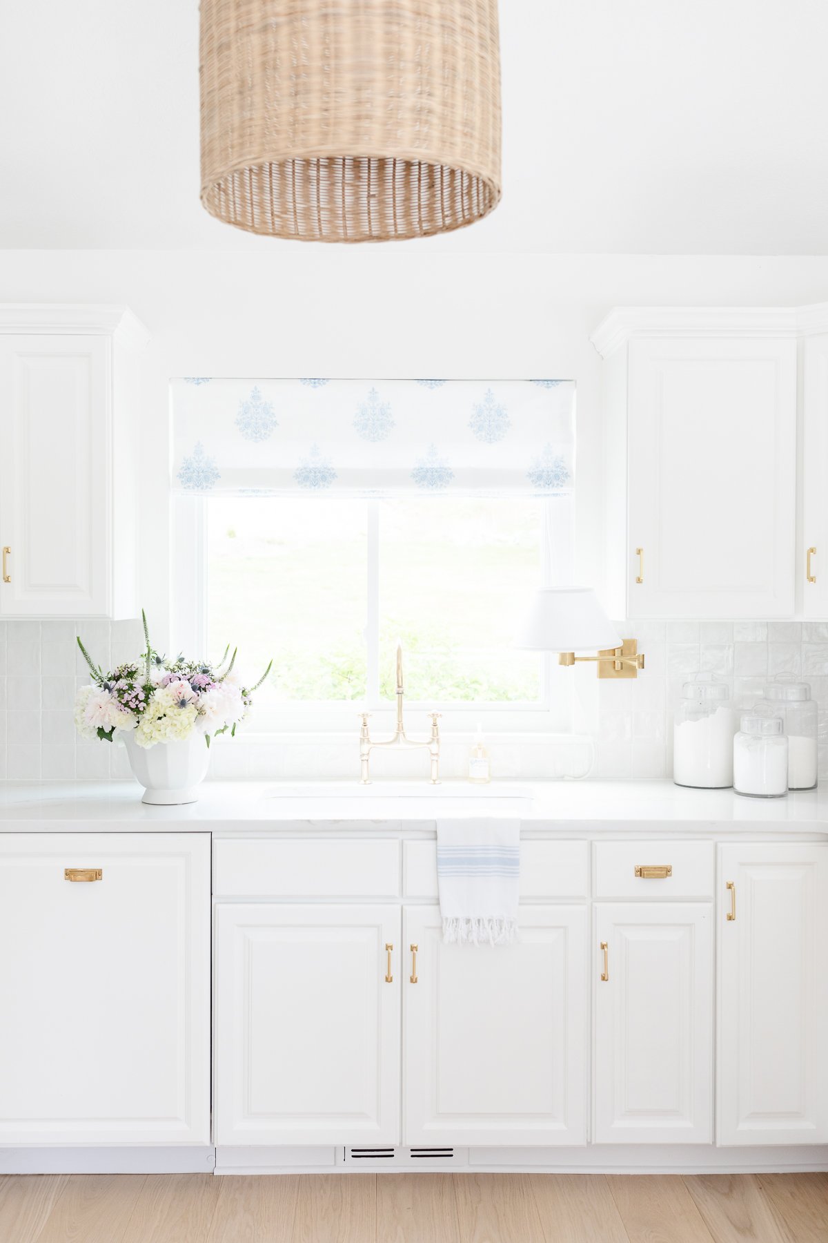 A kitchen with white cabinets and a wicker pendant light. The kitchen counter organization is perfect.