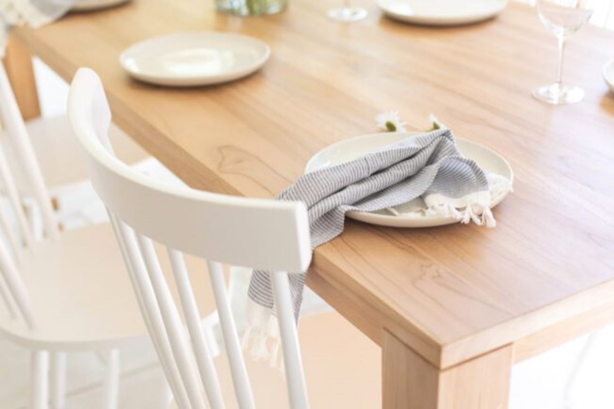A teak dining table with white chairs and plates.