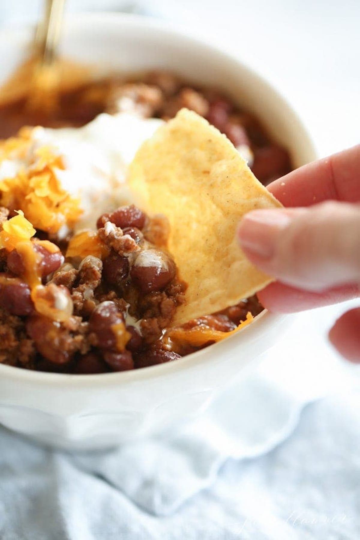 A person quickly dipping an easy tortilla into a bowl of chili.