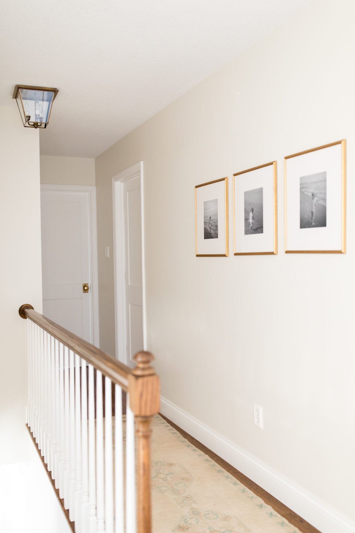A hallway with a white railing and traditional rugs under framed pictures.