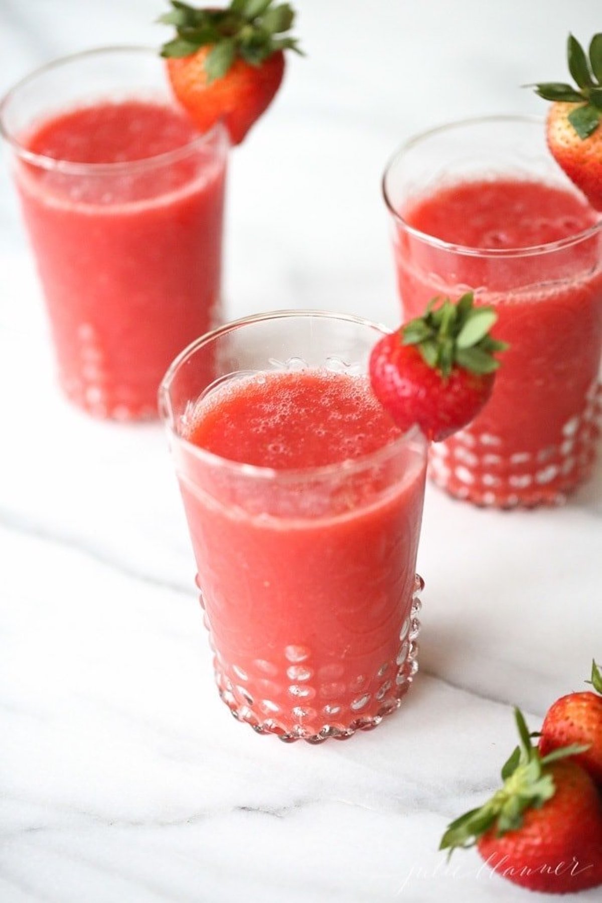 Three glasses of strawberry juice adorned with fresh strawberries, perfect for Valentine's Day recipes.