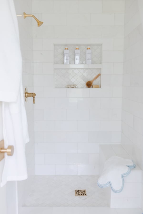 A white tiled shower with a bench and towels.
