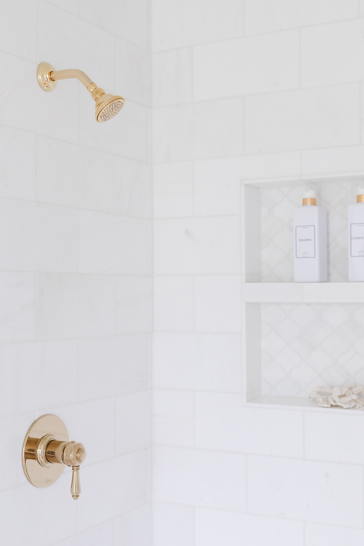 A white bathroom with a gold shower head and shelves.