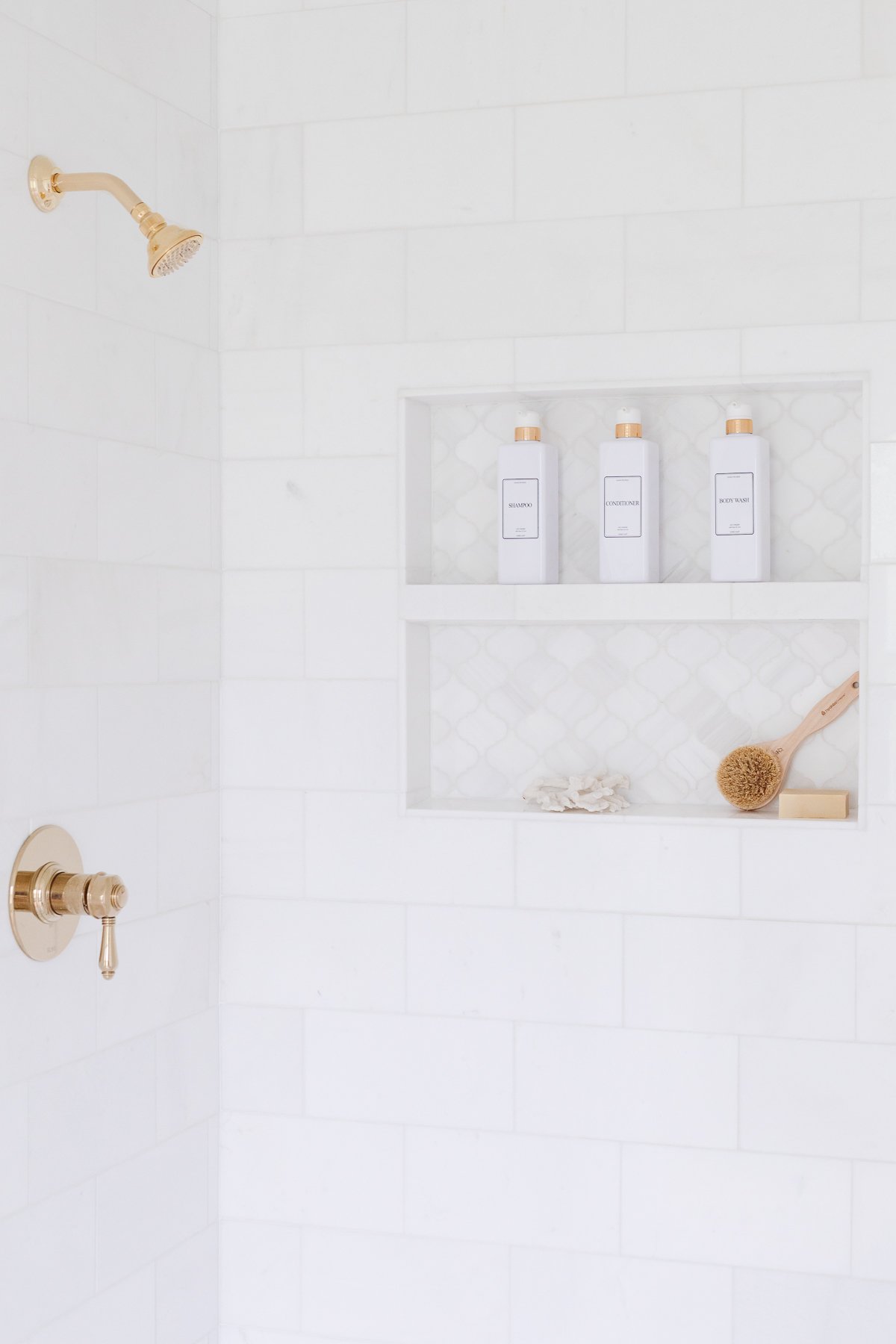 A white tiled shower with a gold shower head.