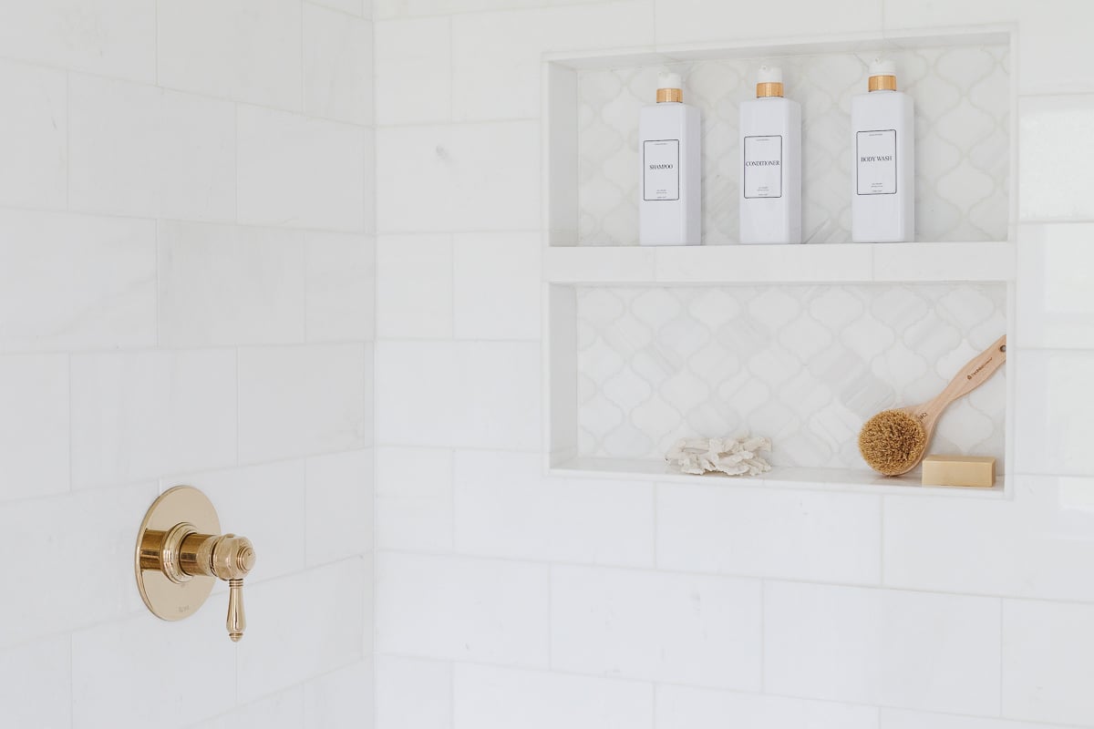 A white tiled shower with a gold shelf.