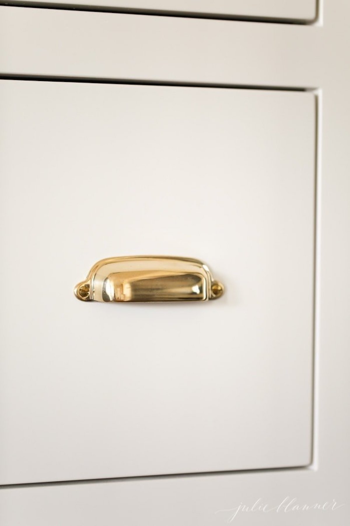 A close up of a gold handle on a white cabinet with shaker cabinet knob placement.