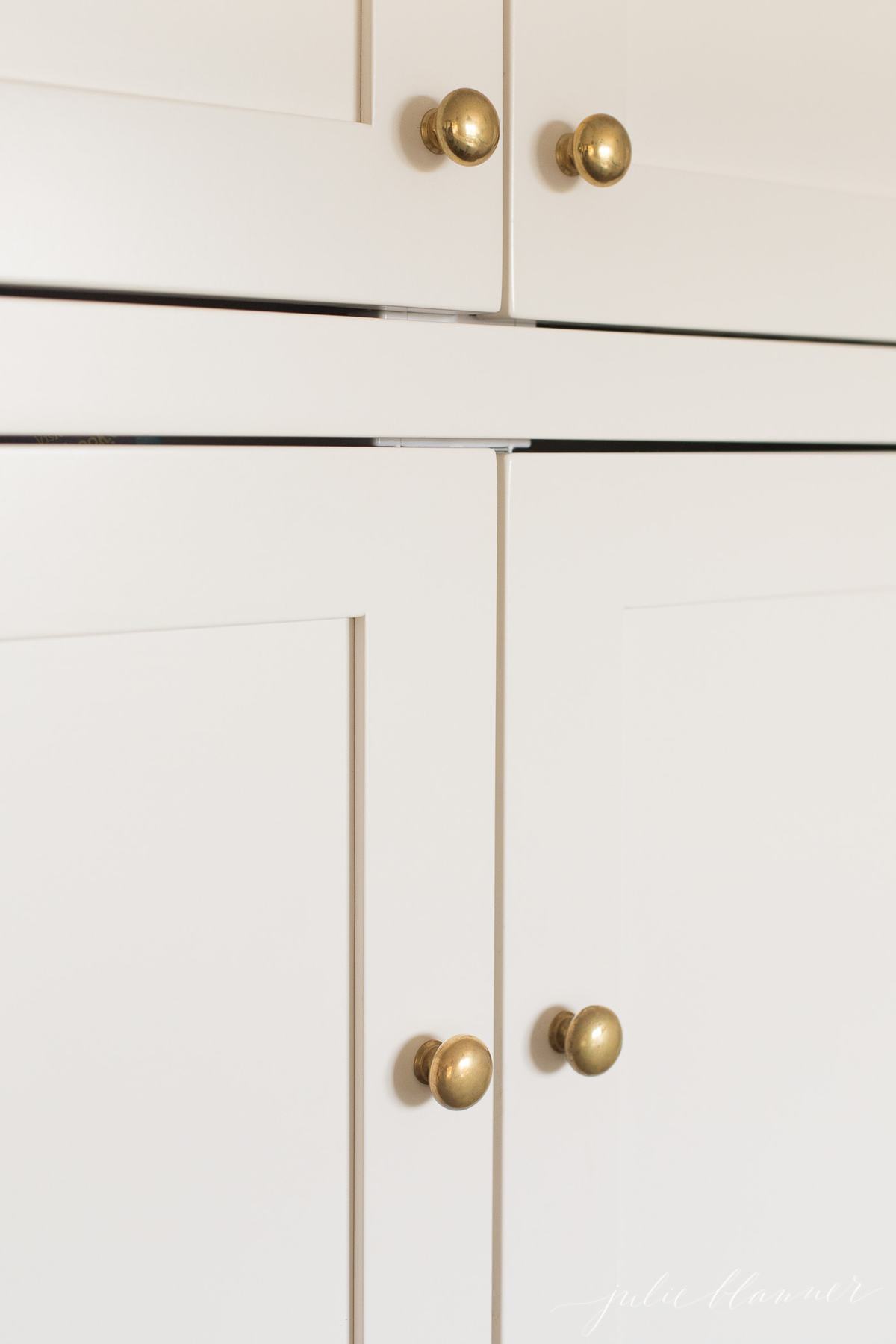 A close up of a white cabinet with brass knobs, showcasing exquisite cabinet door knob placement.