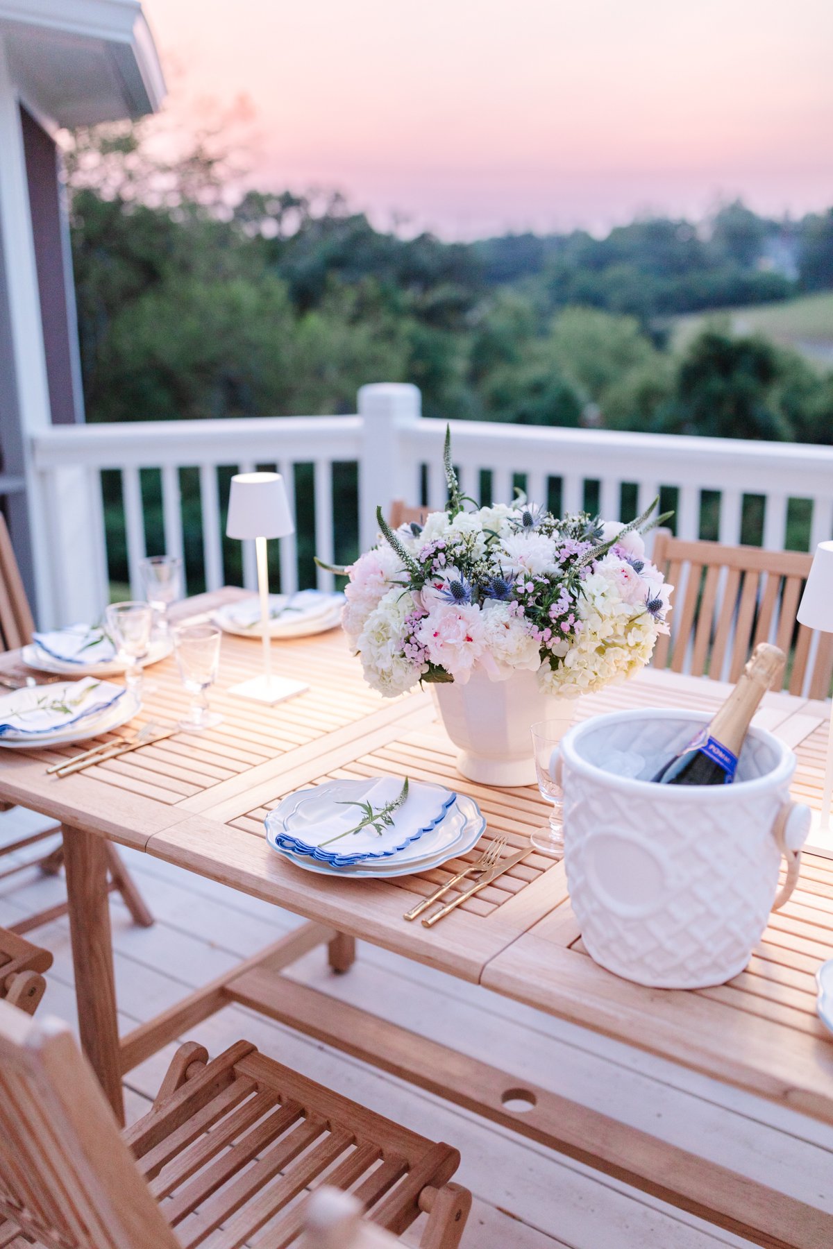 A wooden table set before dinner on a deck at sunset.