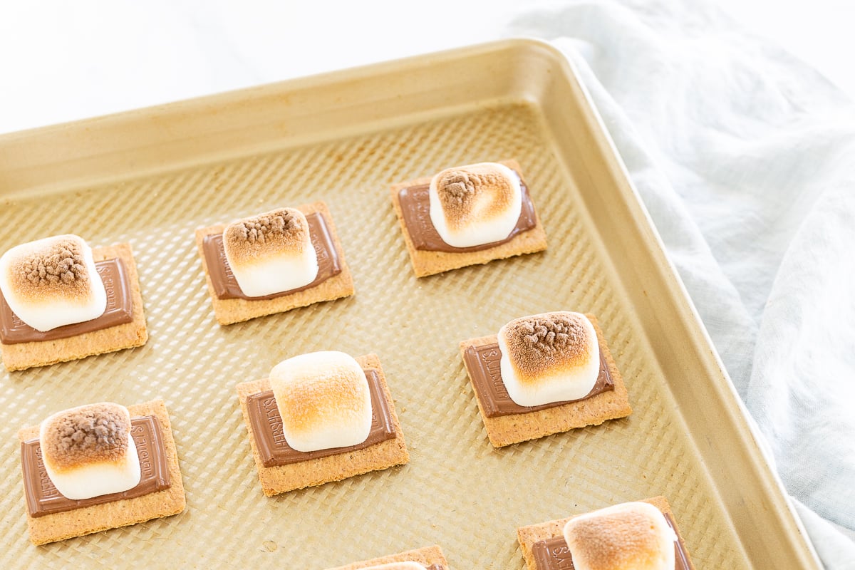 Oven-baked s'mores made with graham cracker squares, marshmallows, and chocolate on a baking sheet.