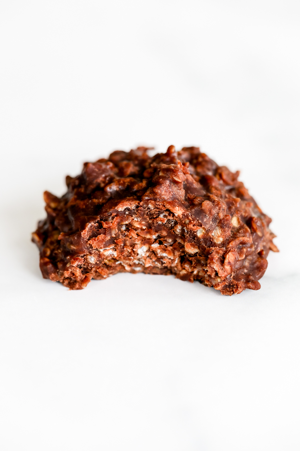 A piece of chocolate cookie, known as a preacher cookie or chocolate no bake cookie, is sitting on a clean white surface.