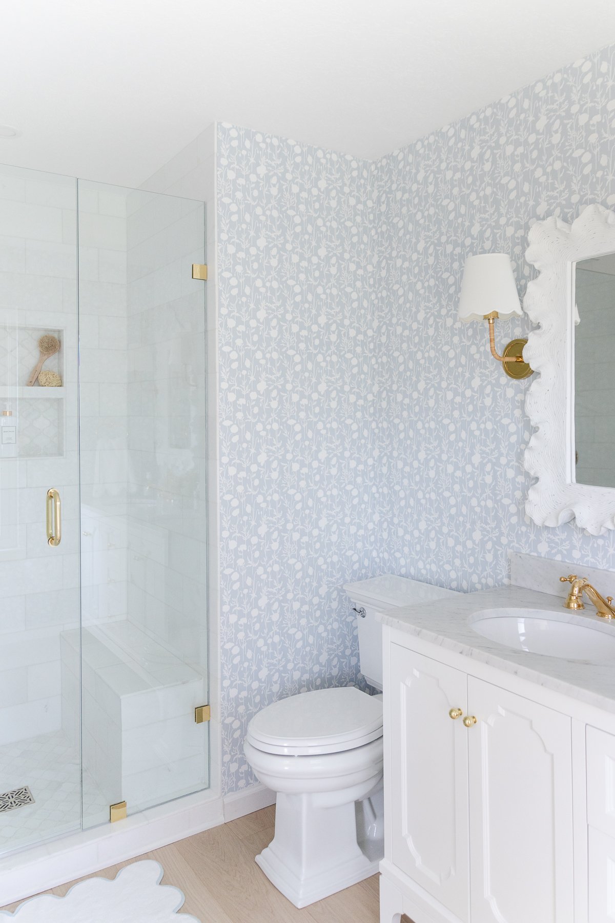 A white bathroom with a glass shower stall featuring Serena and Lily wallpaper.