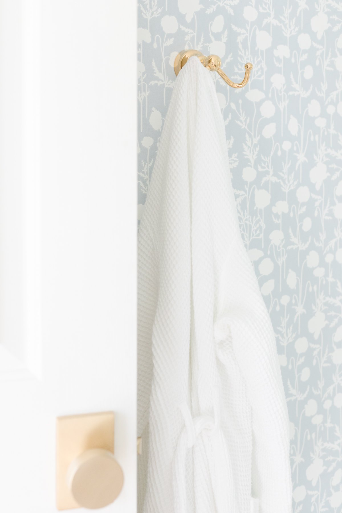 A white towel hangs on a hook in a bathroom featuring Serena and Lily wallpaper.
