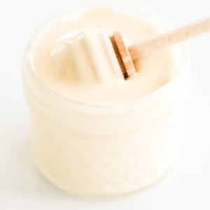 A wooden spoon is pulling whipped honey out of a jar.