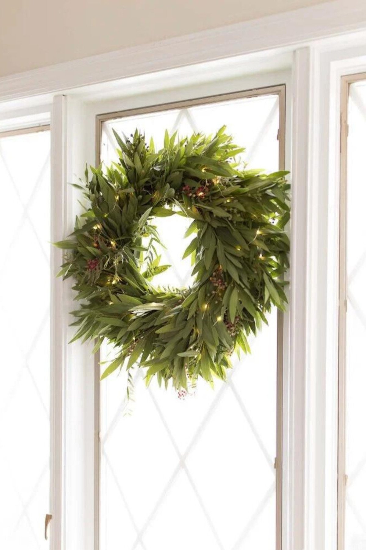 A wreath hanging on a window sill adorned with Christmas lights.