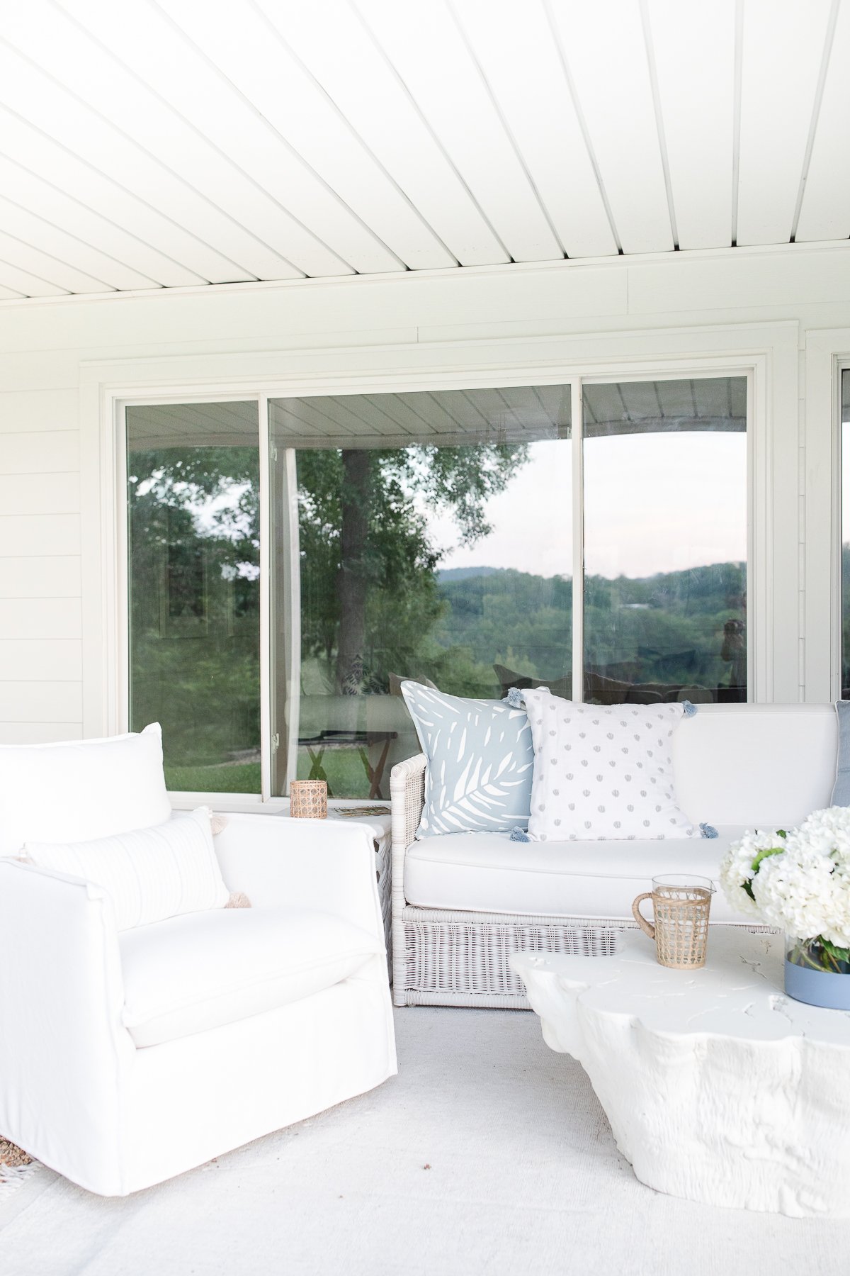 A serene and tranquil outdoor patio featuring exquisite white furniture by Serena and Lily, including a comfortable couch and a stylish coffee table.
