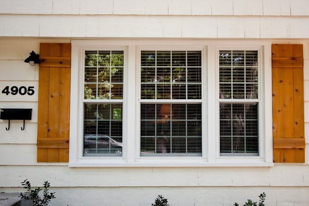 A white house with DIY wooden shutters and a number on the window.