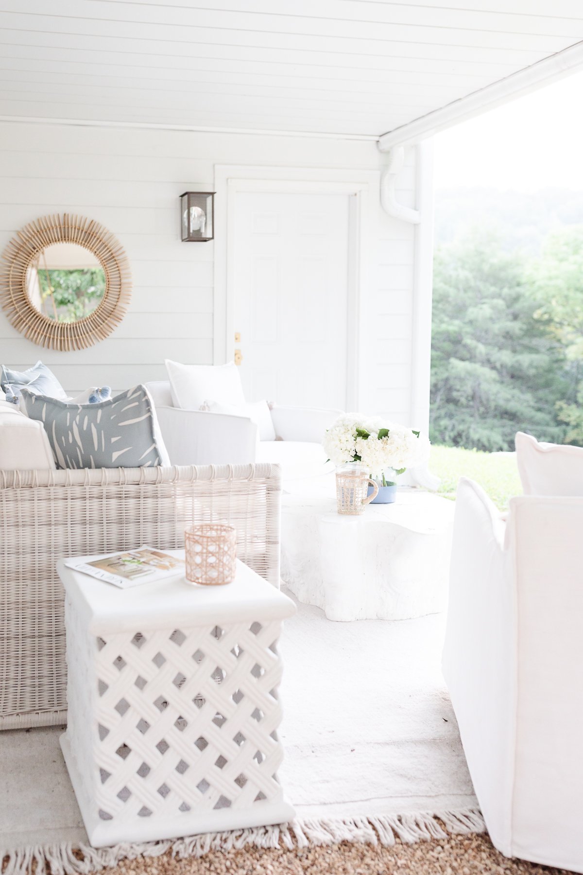 A white porch with [Serena and Lily] wicker furniture and a mirror.