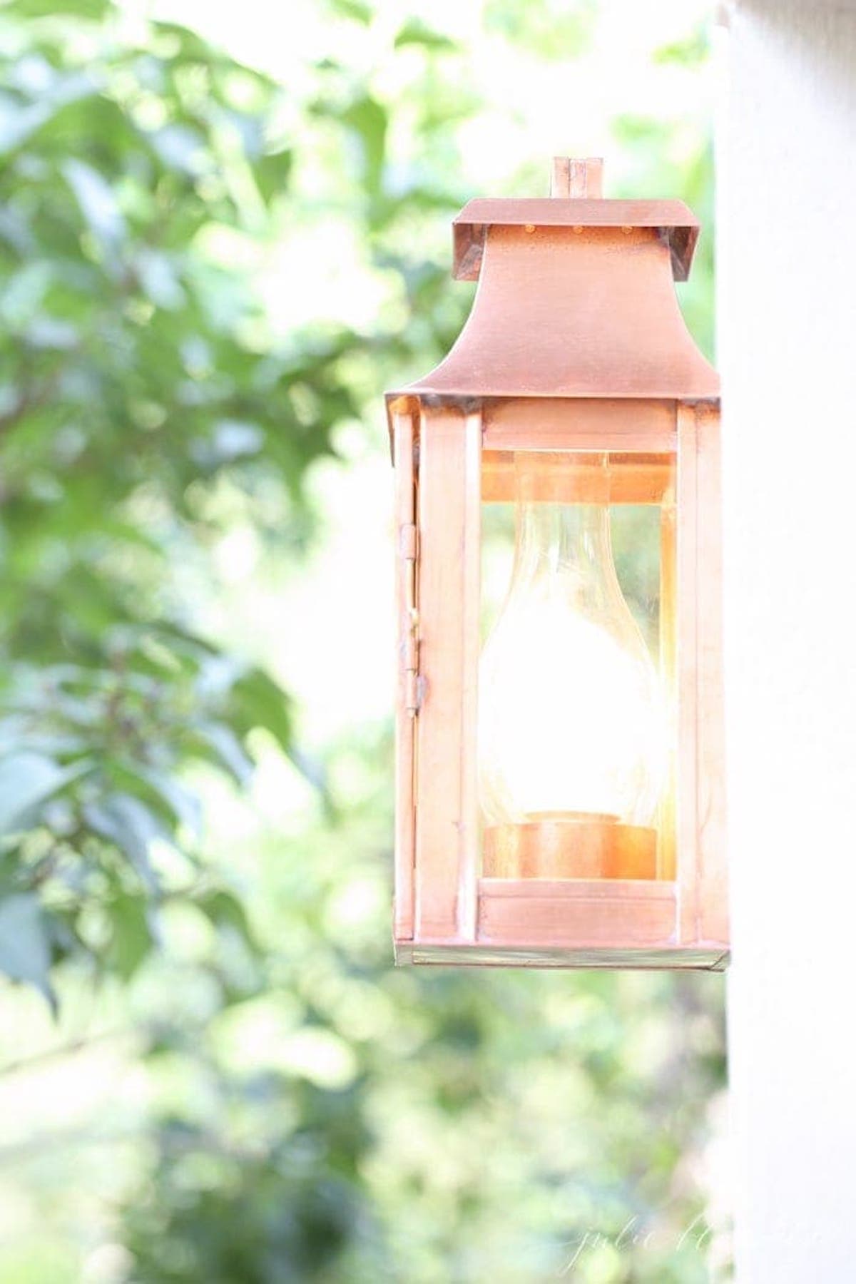 A copper lantern for outdoor lighting, hanging on the side of a house.